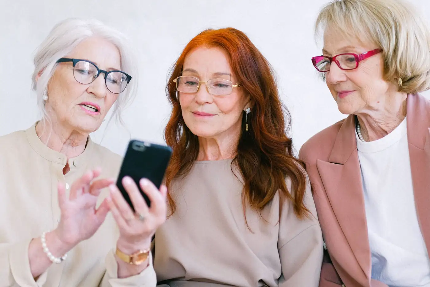 Tres amigas miran juntas una pantalla de móvil y comentan lo que ven.